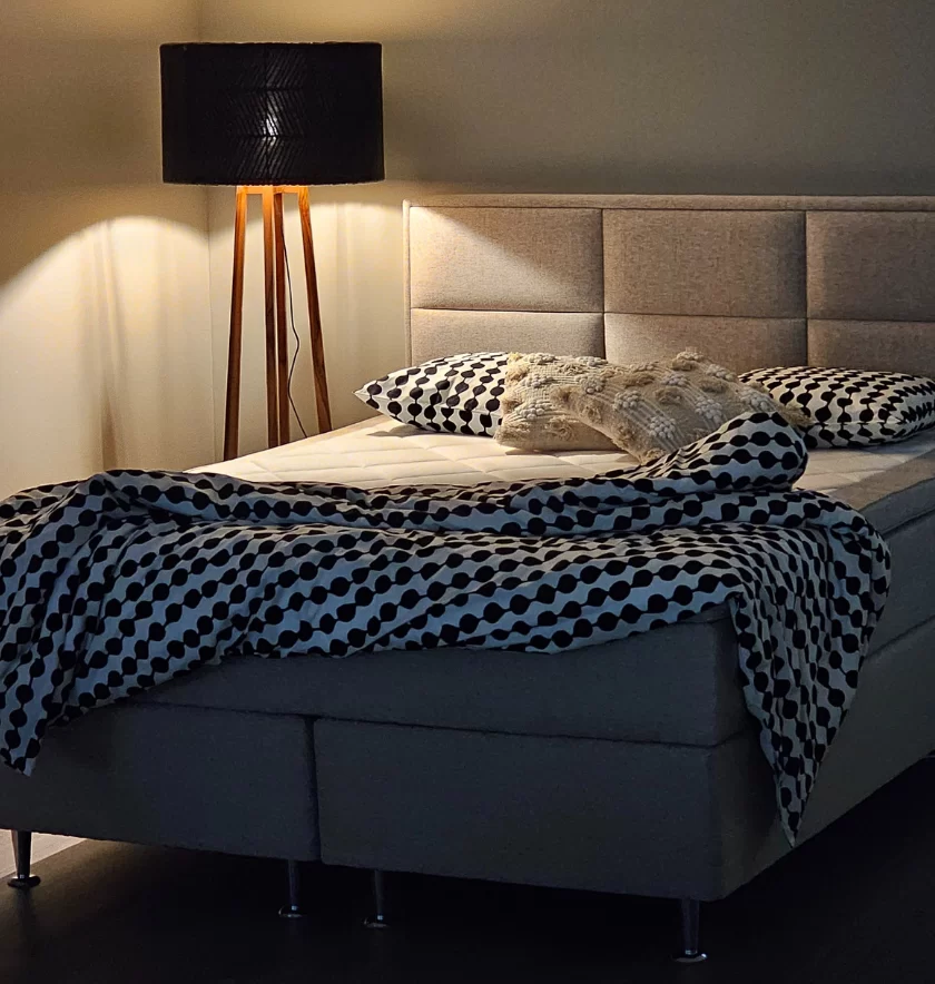 Honey Hotelbeds jenkkisänky tunnelmallisessa huoneessa, mustavalkoisilla vuodevaatteilla, pehmeällä sängynpäädyllä ja lattiavalaisimella