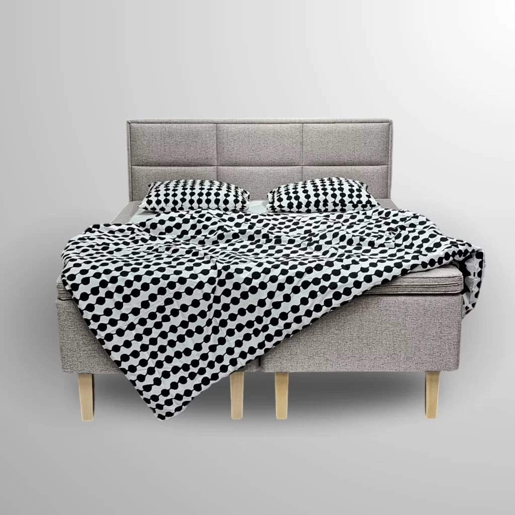 Honey Hotelbeds runkosänky taustattomassa kuvassa, pehmustetulla sängynpäädyllä, vaalealla verhoilulla ja mustavalkoisilla kuviollisilla vuodevaatteilla